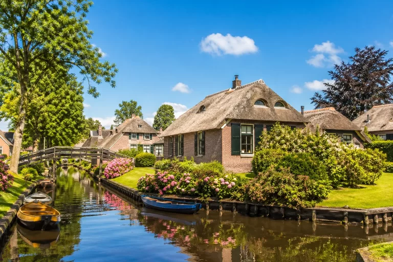 Pittoresk Nederlands dorp met rietgedekte huizen, bloemen en een rustige gracht.